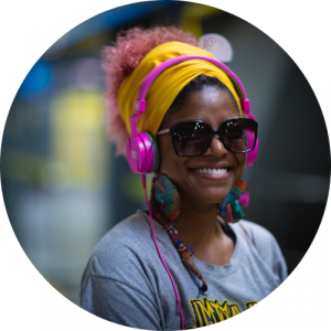 black woman smiling with pink hair wearing sunglasses and pink headphones